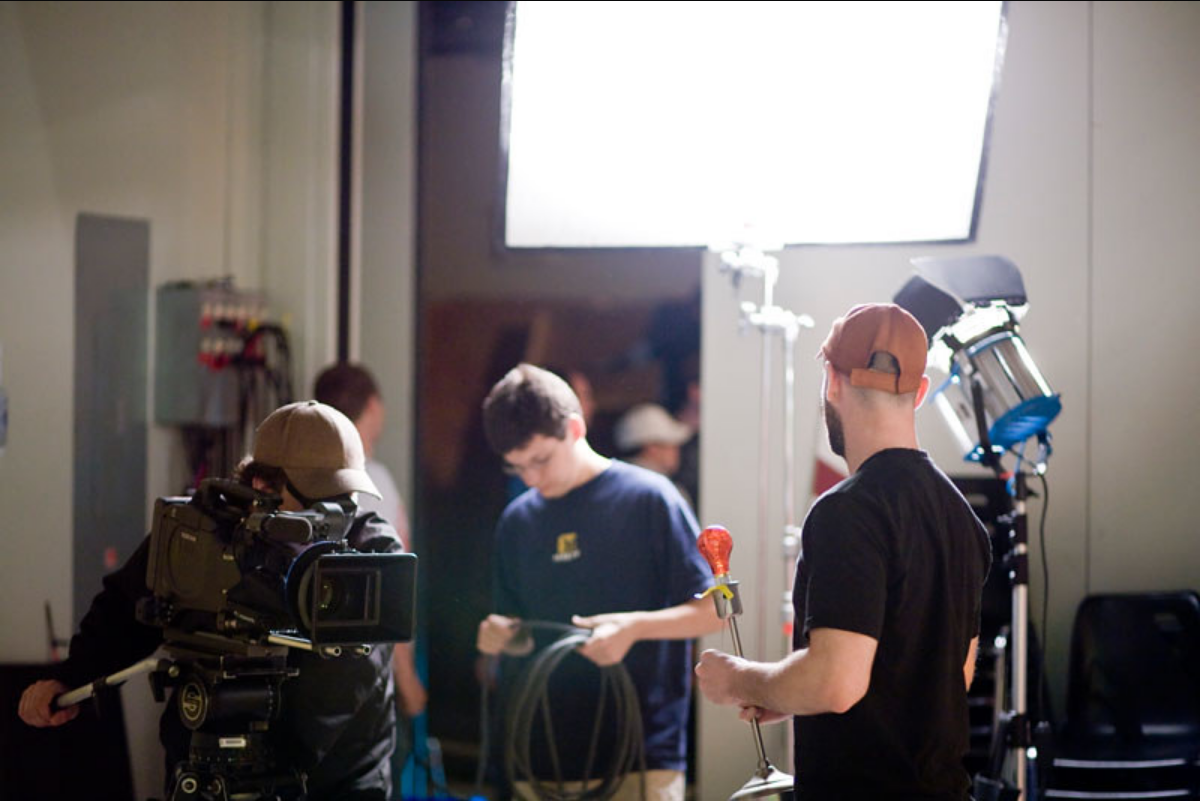 A group of people working together holding different equipment such as camera, cables and lights.