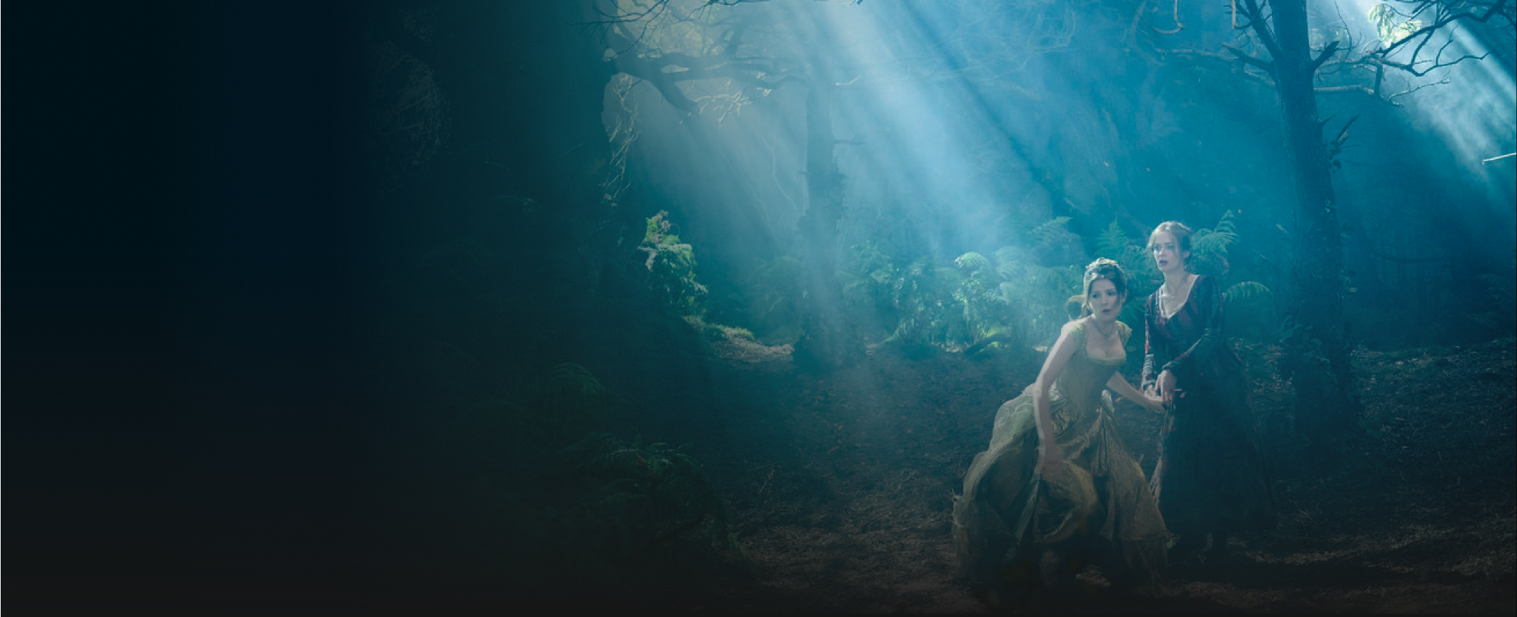 Two women looking distraught in old fashioned dresses in a dark forest
