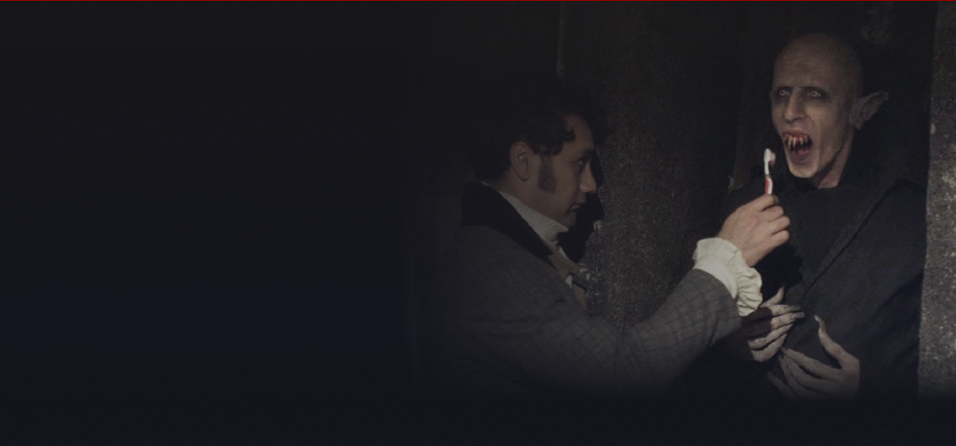 A young man dressed old-fashioned brushing a old, bald and pale vampire's teeth while it's in a casket.